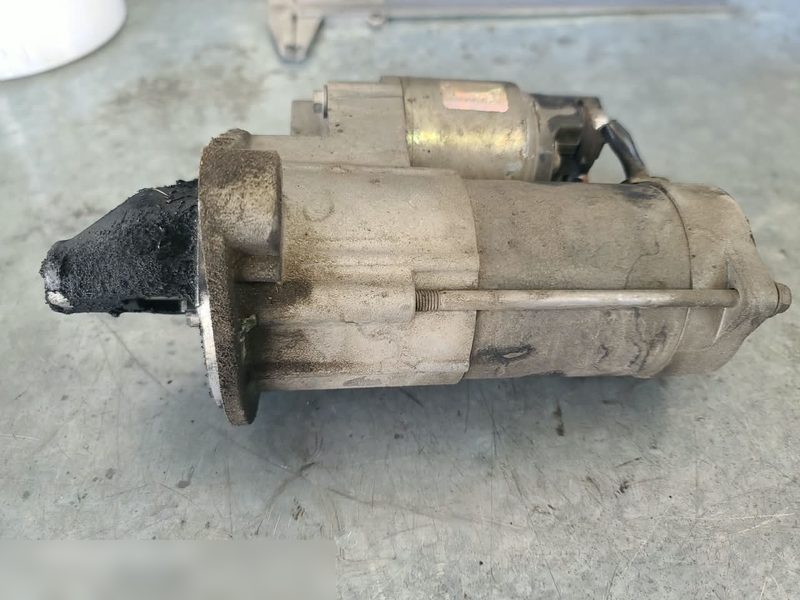 Motor de arranque desmontado, apoyado en el piso del taller